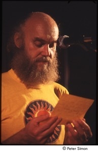 Ram Dass reading from piece of paper, on stage with Amazing Grace