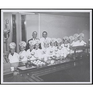 Members of the Tom Pappas Chefs' Club pose in a cafeteria with Boys' Club of Boston Assistant Executive Director Louis Zeramby and Brandeis University Director of Dining Halls and Chef's Club Committee member Norman R. Grimm
