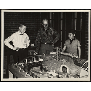 A Man and two boys observing the layout of their model railroad