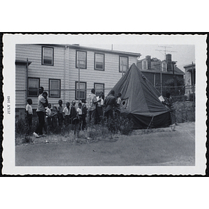 A group of boys stand on line to enter a tent pitched in a yard during Tom Sawyer Day