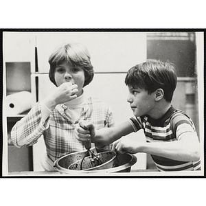 A boy mashes berries as a girl samples one in a kitchen