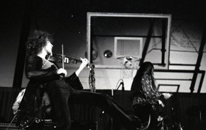 Unidentified band in performance in what appears to be a high school gymnasium: violinist and lead singer