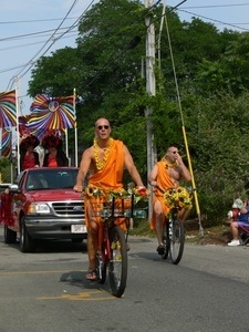 Men with shaved head and dressed in a saffron robe bicycling in the parade: Provincetown Carnival parade