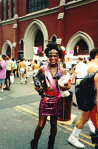 A Photograph of Marsha P. Johnson Holding Bags, Wearing a Sequined Skirt and a Pink “Stonewall” Sash