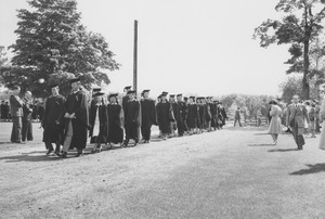 Faculty leading an outdoors procession of graduates to Curry Hicks Cage