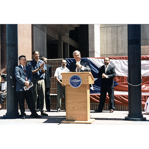 Mayor Thomas Menino speaks from a lectern with men standing around him