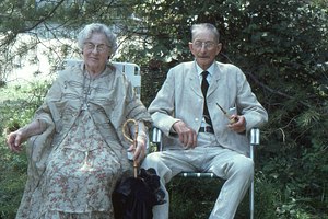 Ella and Arthur Rosenburg sitting in lawn chairs at Moon Barn Raising at entrance to Hopkins Forest on 2 August 1975. Steven Masters in straw hat at left.
