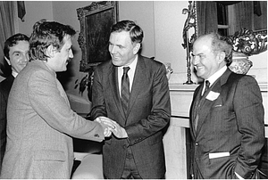 Mayor Raymond L. Flynn embracing the hand of an unidentified man with others watching on