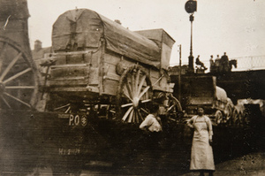 Two civilians standing in front of covered wagons being transported on railroad flat cars