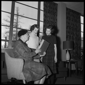 Eleanor Roosevelt (left) seated in the Cape Cod Lounge (Student Union), reading a book report presented by two young girls, during Roosevelt's Distinguished Visitors Program appearance at UMass Amherst