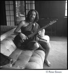 Krishna Das, playing bass guitar, sitting on a couch in the Vicente Street house