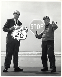 Two unidentified men posing with road signs on a beach