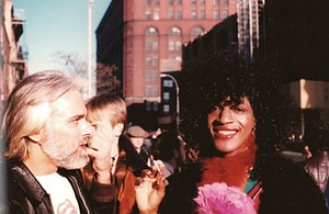 A Photograph of Marsha P. Johnson Wearing Red Lipstick, a Red Feather Boa, a Pink Flower, and Smoking a Cigarette