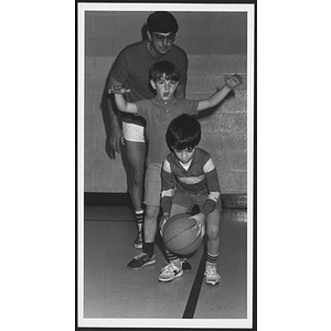 Man helps two boys learn to dribble during basketball instruction