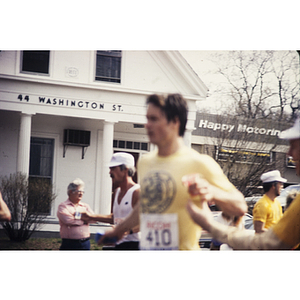 Runners pass crowd and white building on Washington St. during Boston Athletic Association (BAA) marathon