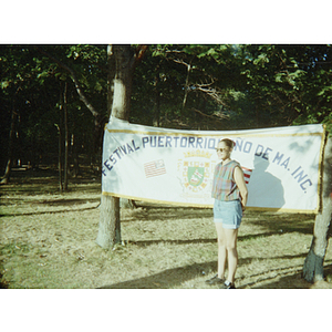 A woman stands in front of a Festival Puertorriqueño banner at a picnic event