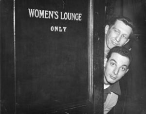 Two male Suffolk University students peering out of door marked "Women's Lounge Only"