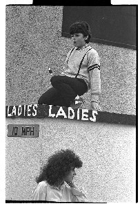 Young man on roof of "Ladies'" as a woman walks out