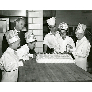 "John Frost and John Power of the Bunker Hill Club help to decorate the birthday cake donated by Peter De Dominici, celebrated cake decorator, for the governor's birthday party which he will celebrate at the Bunker Hill Boys Club on Monday, March 28 at 3:30. Mrs. Herter and 150 boys and girls will be on hand to celebrate w/ the honored guest." Assistant Executive Director Louis Zeramby stands far left