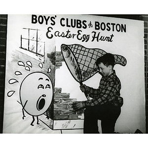 A boy poses with a large, interactive poster that reads "Boys' Clubs of Boston Easter Egg Hunt"