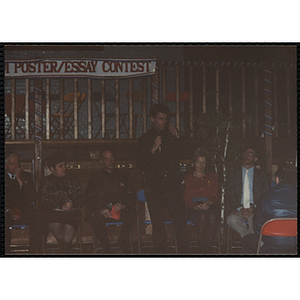 A man speaking into a microphone while several guests sit behind him at the MADD 1991 Poster and Essay Contest