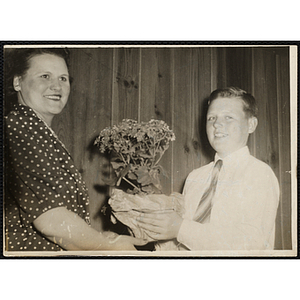 A boy in a shirt and tie presents flowers to a woman during a Boys' Club event