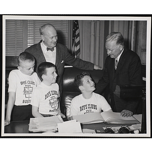 Executive Director of Boys' Clubs of Boston Arthur T. Burger (left) and Mayor John B. Hynes (right) stand at a desk with three boys