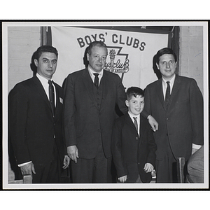 Three men and a boy pose in front of a Boys' Clubs banner
