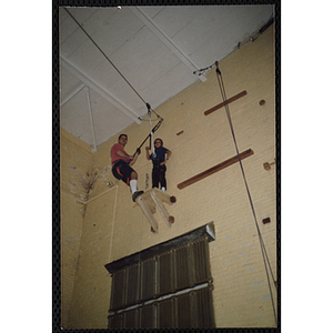 A boy and an indoor climbing supervisor stand on a platform in a gymnasium