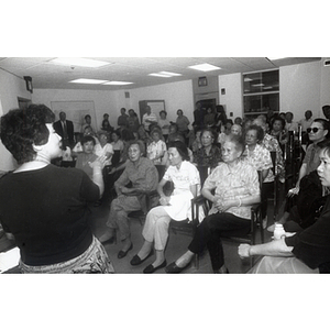 Woman addresses a group of members, who are seated facing her