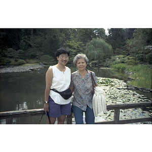 Suzanne Lee and another Association member stand on a bridge over a small pond during a visit to a park