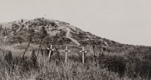 Three wooden crosses in a grassy field and more crosses on the top of a small hill in the background, Butte de Warlencourt