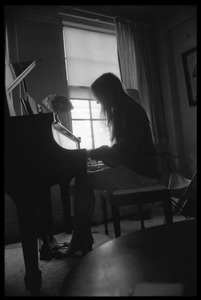 Judy Collins silhouetted against a window, playing piano in her New York apartment