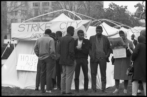 Strikers and supporters milling about outside a tent, a woman reading a newspaper