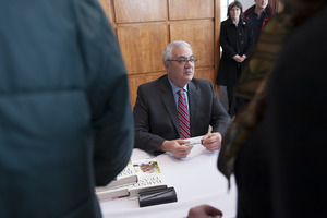 Congressman Barney Frank seated at a table in the Student Union Ballroom stage, UMass Amherst, signing copies of his biography