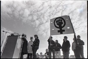 Anti-war rally at Soldier's Field, Harvard University: members of feminist group Bread and Roses wearing masks, speaking and holding a fist in a venus symbol