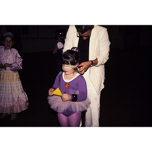 Adult putting a blindfold on a young girl in a ballet costume