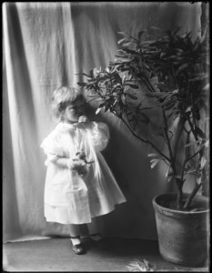 Child holding toy standing beside potted plant