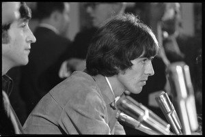 George Harrison in front of a bank of microphones, in profile, during a Beatles press conference