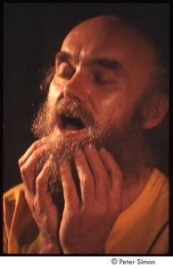 Ram Dass with his hands on his beard, on stage with Amazing Grace