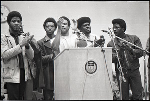Huey P. Newton speaking at Boston College: Newton at podium with Party members, including David Hilliard (2nd from left) and Elbert Howard (2rd from right)