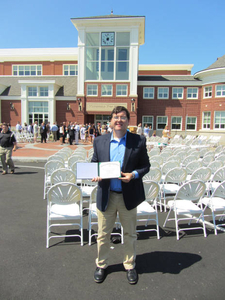 Peter Woods holding associates degree in front of new MHS