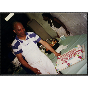 A man wearing an apron looks at a cake commemorating the "BEST-YEAR-IN SCHOOL-EVER RECOGNITION DINNER MAY 22nd 1991"