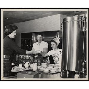 A member of the Tom Pappas Chefs' Club serves coffee to a woman in a Brandeis University dining hall as a staff person looks on