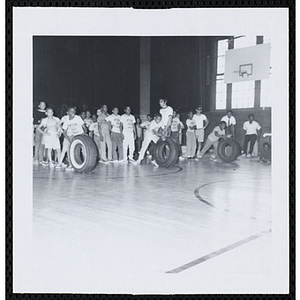Three boys prepare to compete in a tire rolling race in a gymnasium on Tom Sawyer Day