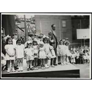 A man standing with the contestants and their brothers on the outdoor stage at a Boys' Club Little Sister Contest