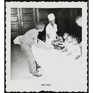 Two boys serve food and drinks to three girls sitting at a table during a Boys' Club Little Sister Contest
