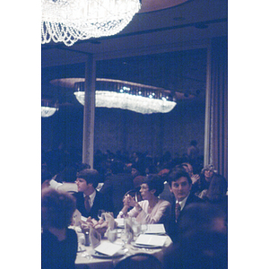 People sit at a dinner table in a large banquet hall during an unidentified formal event