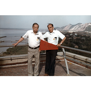 Two male Association members hold a red flag while standing on an observation deck