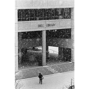 A student walks toward Snell Library as it snows